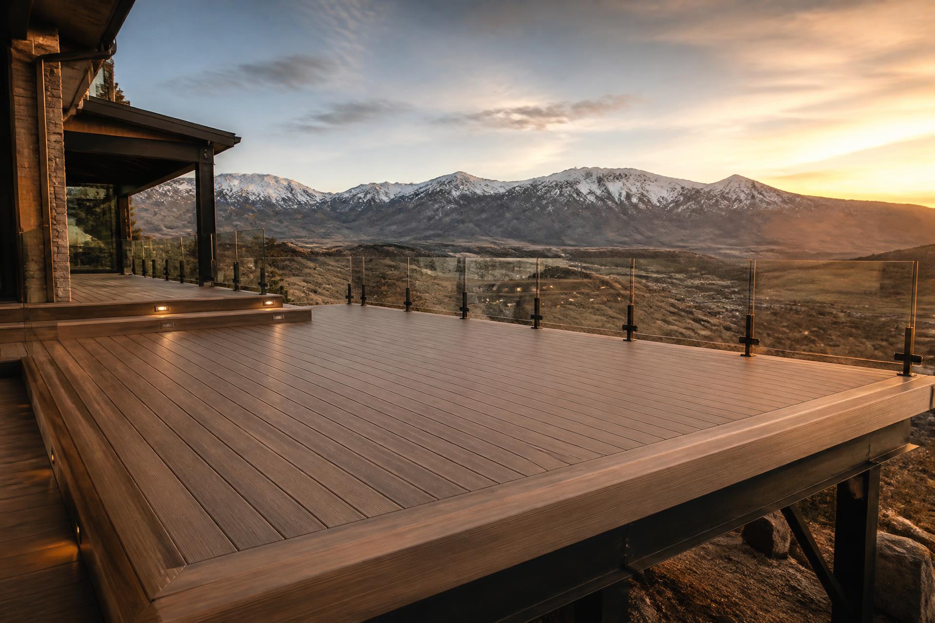 Custom-built luxury deck in Utah showing picture-framed decking, glass guardrail, and mountain-modern structural detail at sunset